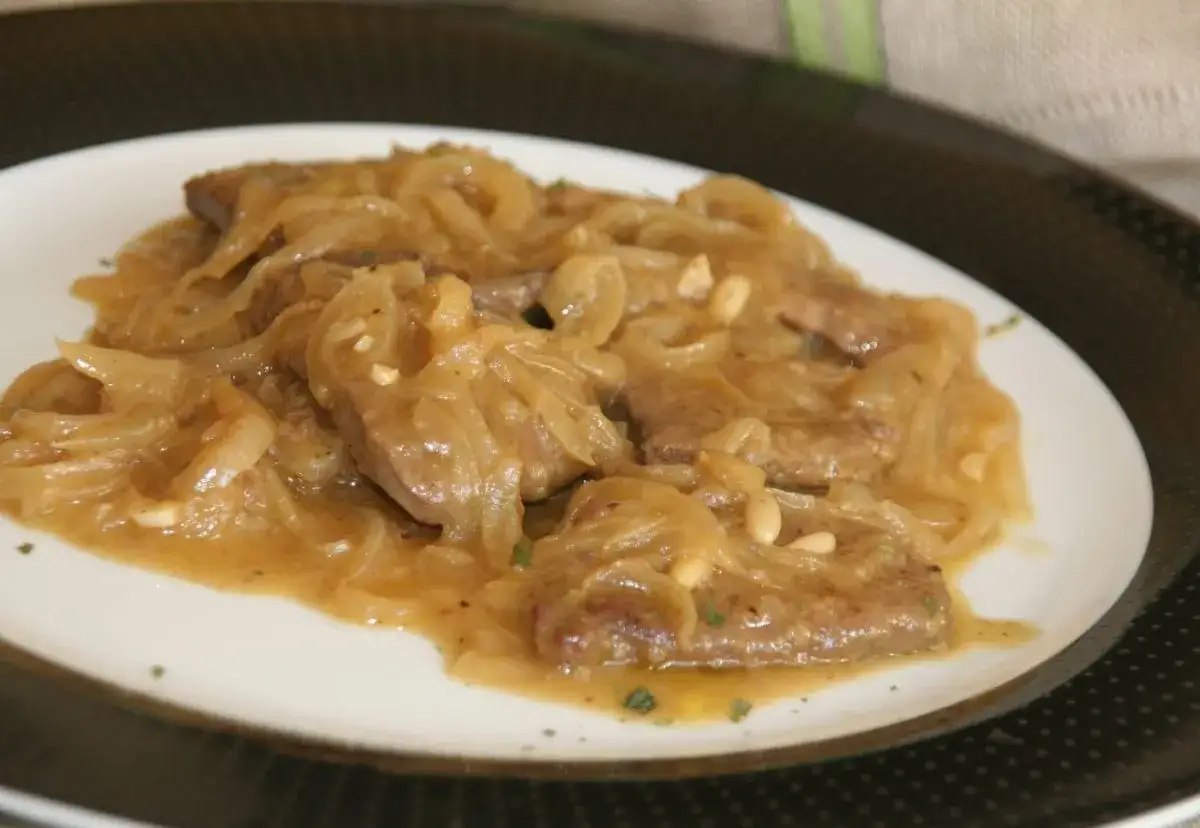 Delicioso plato de h&iacute;gado encebollado, tierno y jugoso, con cebolla caramelizada y pi&ntilde;ones.