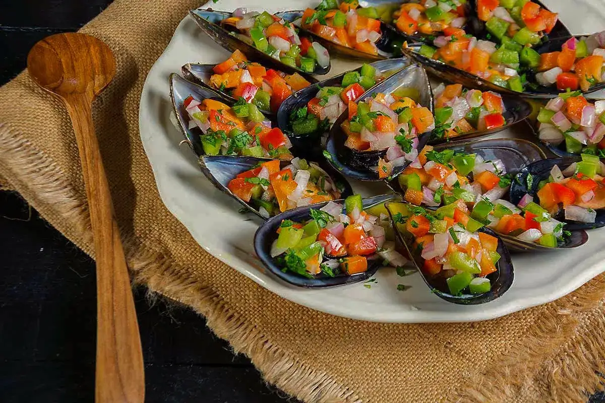 Mejillones a la vinagreta, frescos y coloridos, servidos en sus conchas con una mezcla de pimientos y cebolla picados.