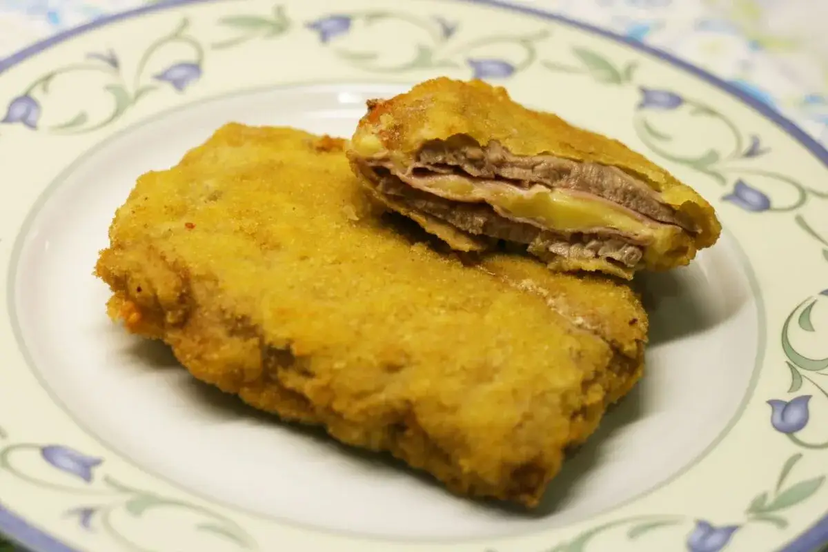 San Jacobo dorado y crujiente, relleno de jamón y queso fundido, servido en un plato blanco con decoraciones florales.