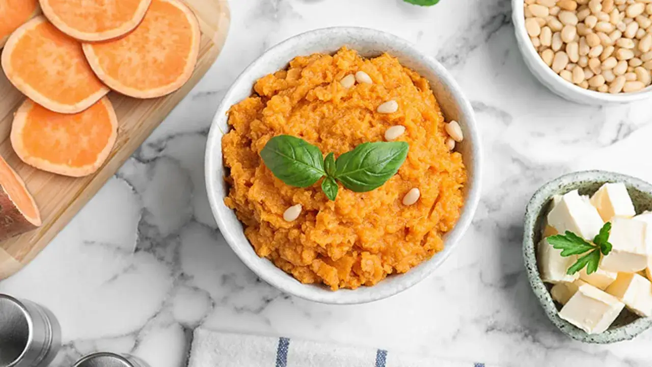 Un cremoso pur&eacute; de boniato adornado con pi&ntilde;ones y albahaca, junto a cubos de queso y rodajas de boniato fresco.