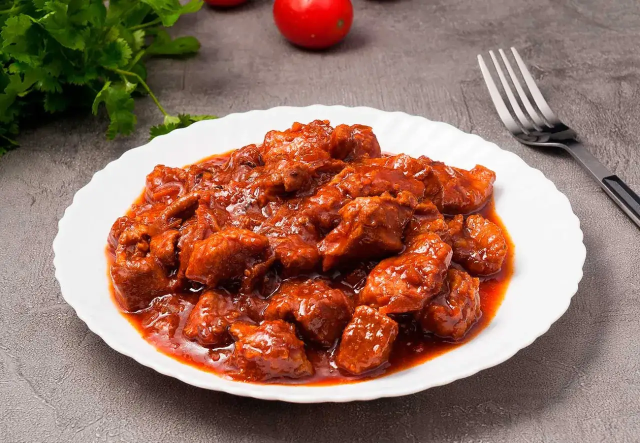 Sabroso magro con tomate, trozos de carne tierna en una salsa roja apetitosa, servido en un plato blanco.