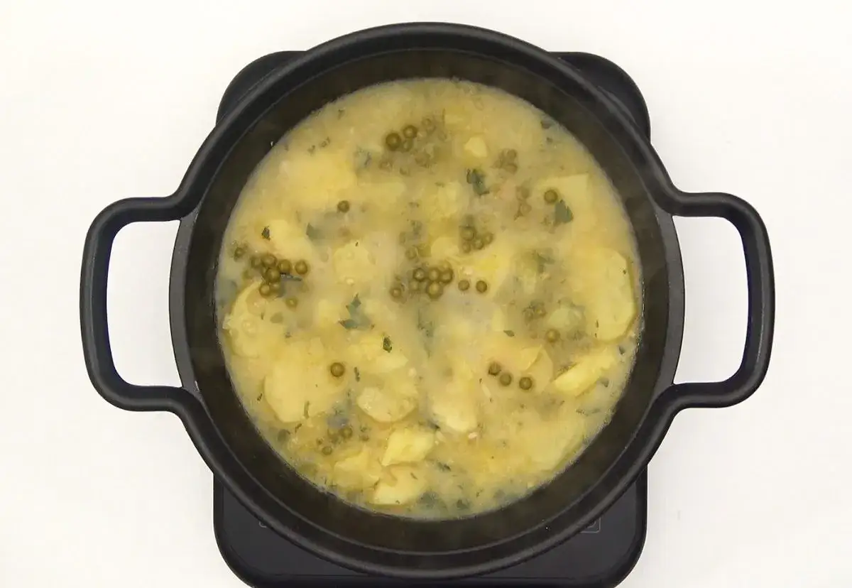 Patatas en salsa verde, con guisantes y perejil, burbujeando en una cazuela negra.