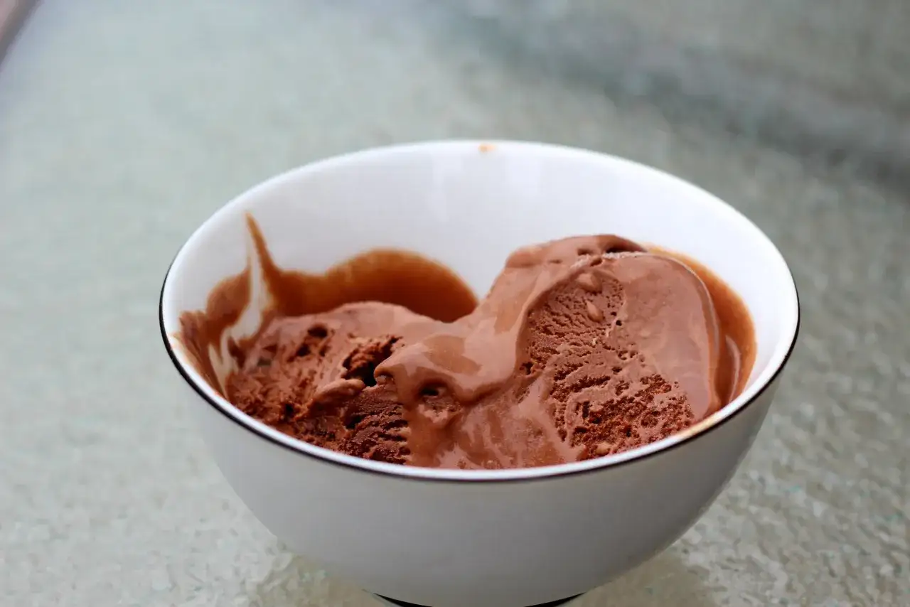 Un taz&oacute;n blanco con un borde dorado contiene cremoso helado de chocolate, con algunas partes derriti&eacute;ndose.