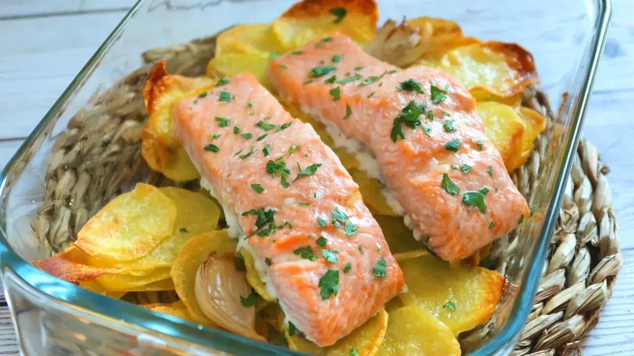 Dos filetes de salm&oacute;n al horno con patatas crujientes y perejil picado, servidos en una fuente de vidrio.