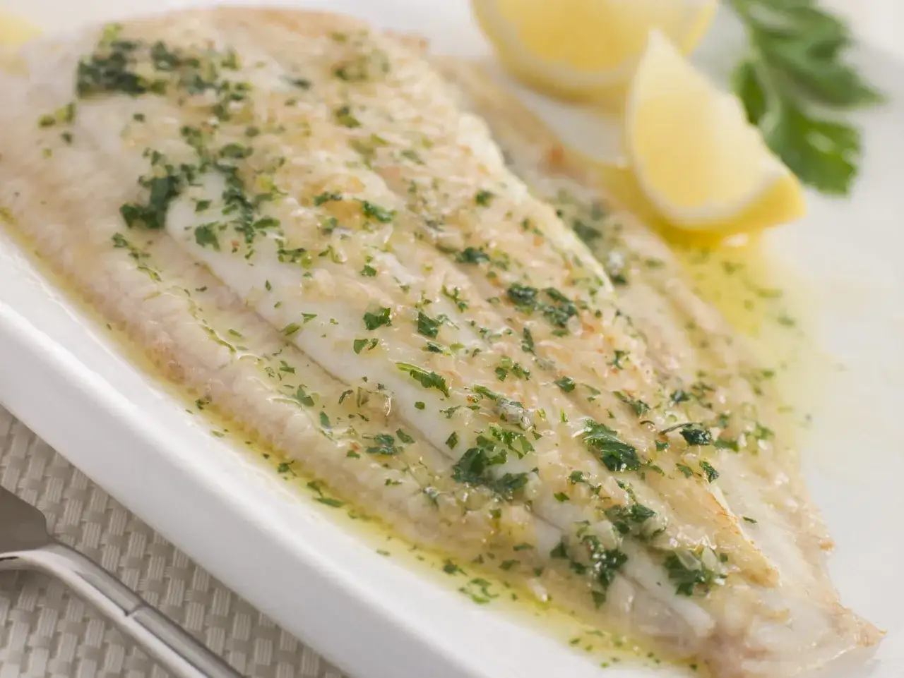 Delicioso lenguado a la meuni&egrave;re, ba&ntilde;ado en mantequilla dorada y perejil fresco, acompa&ntilde;ado de gajos de lim&oacute;n.