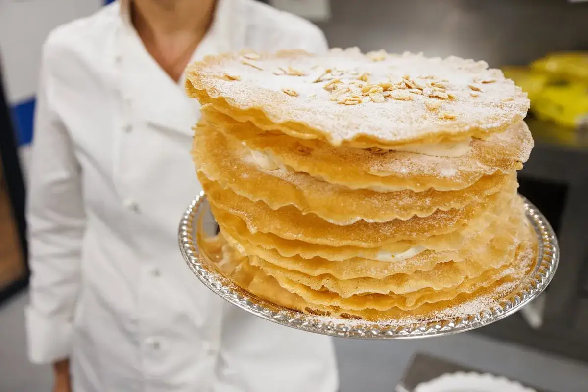 Una tarta &aacute;rabe de varias capas, cubierta de az&uacute;car glas y almendras, servida en un plato plateado.