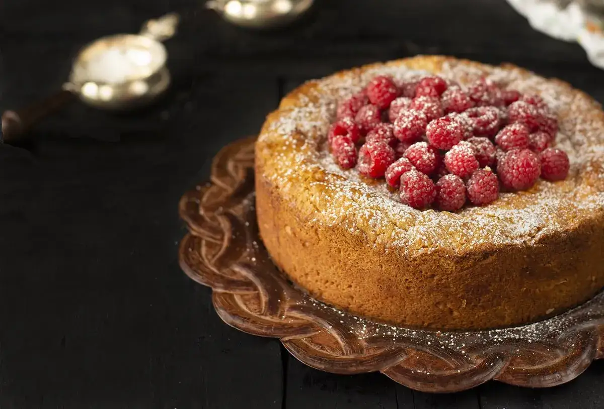 Delicioso pastel vasco cubierto de frambuesas frescas y az&uacute;car glas, servido en un plato decorativo.