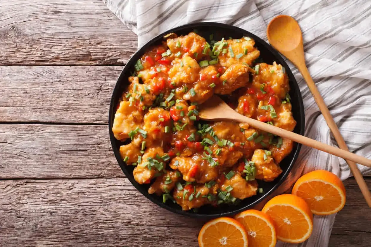 Delicioso pollo a la naranja, crujiente y ba&ntilde;ado en una salsa dulce y c&iacute;trica, adornado con ceboll&iacute;n fresco.