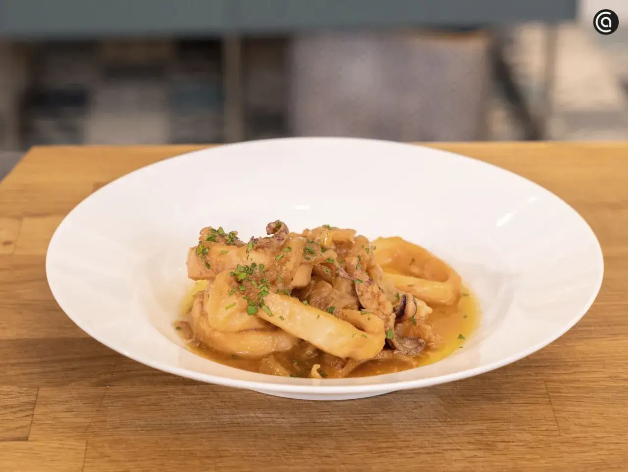 Calamares encebollados, un plato tradicional espa&ntilde;ol, servido en un cuenco blanco sobre una mesa de madera.