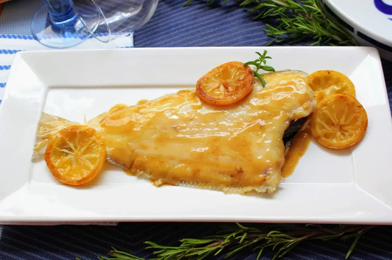 Delicioso gallo a la plancha bañado en salsa dorada, decorado con rodajas de limón caramelizado y ramitas de romero fresco.