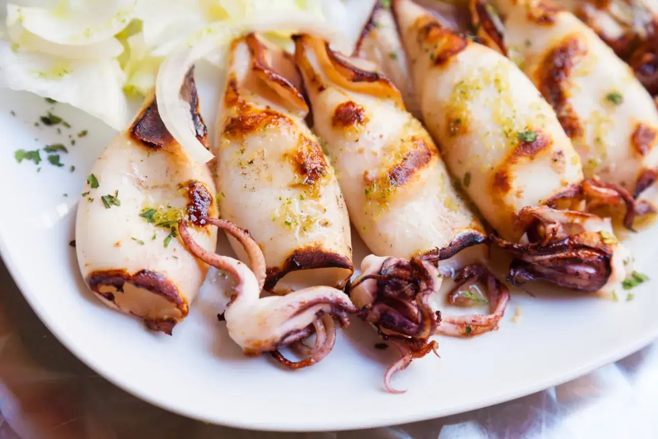 Calamar a la plancha, un pescado blanco tierno y jugoso, servido con aros de cebolla y perejil picado.