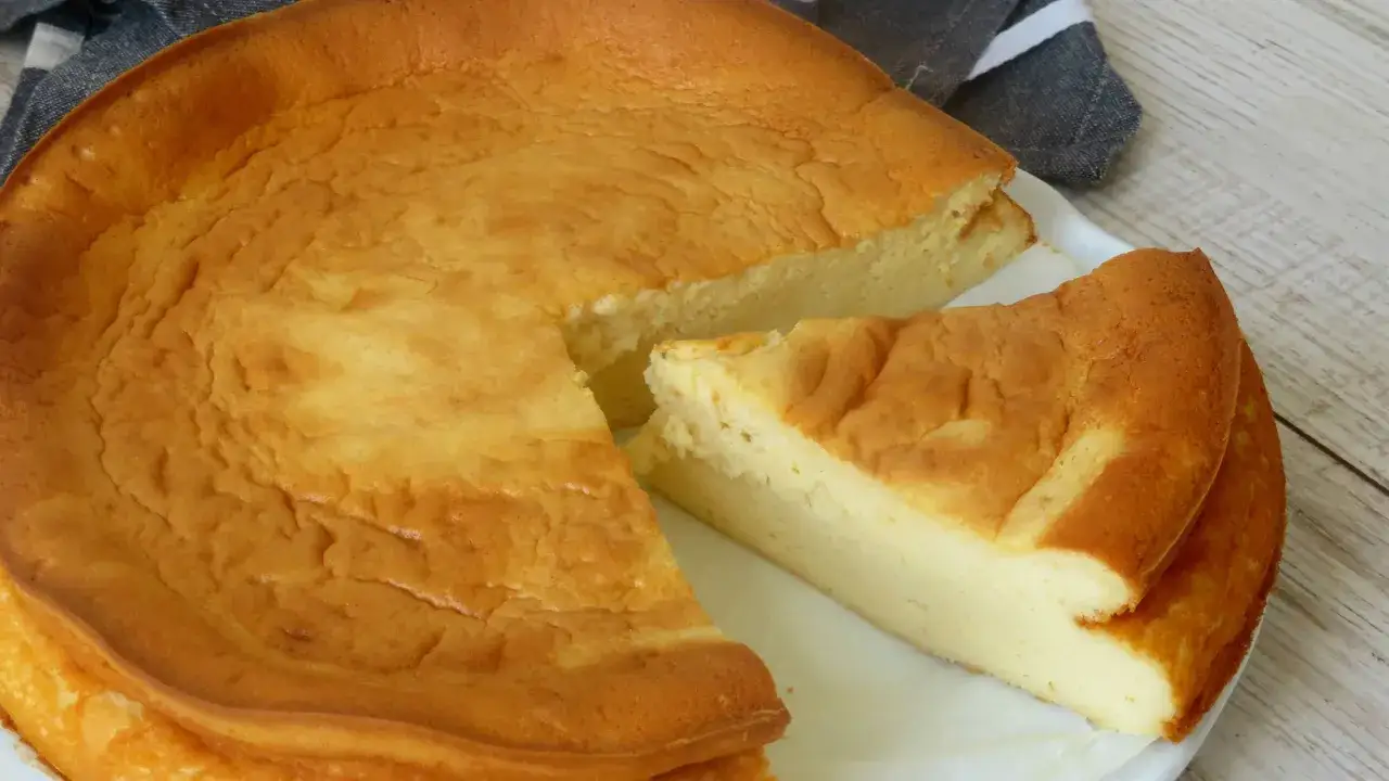 Tarta de queso al horno casera, dorada y esponjosa, con una porci&oacute;n lista para disfrutar.