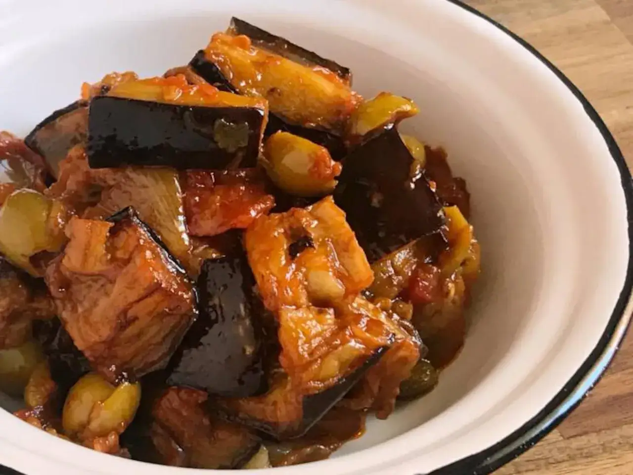 Un plato de caponata siciliana, con berenjenas, aceitunas y tomate, servido en un cuenco blanco.