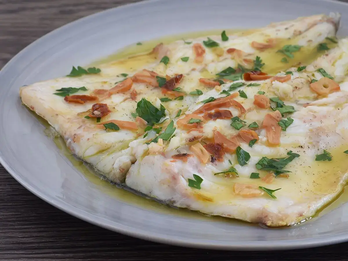 Delicioso lubina a la donostiarra, con l&aacute;minas de ajo dorado y perejil fresco, servida en una salsa aceitosa.
