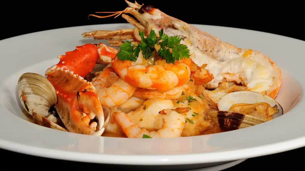 Delicioso rape a la marinera con gambas, cigalas, almejas y pinza de cangrejo, adornado con perejil fresco.
