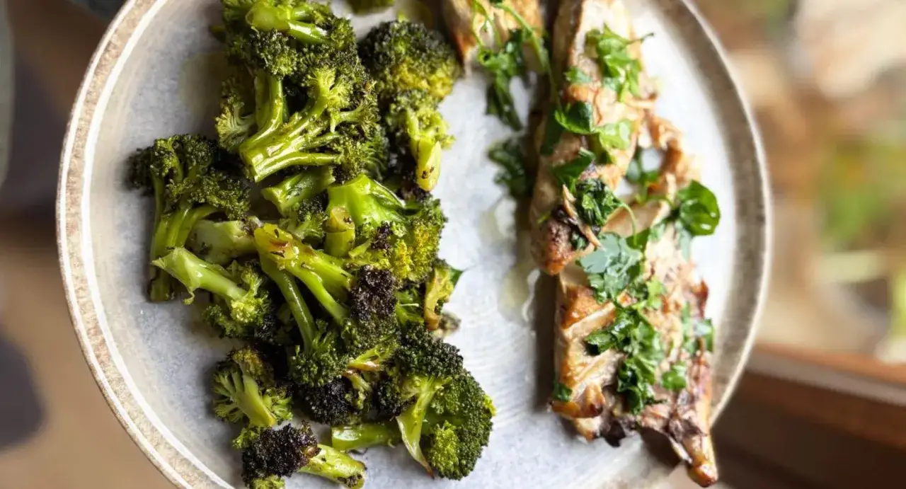 Brocoli al horno, tierno y dorado, servido junto a un filete de pescado con hierbas frescas.