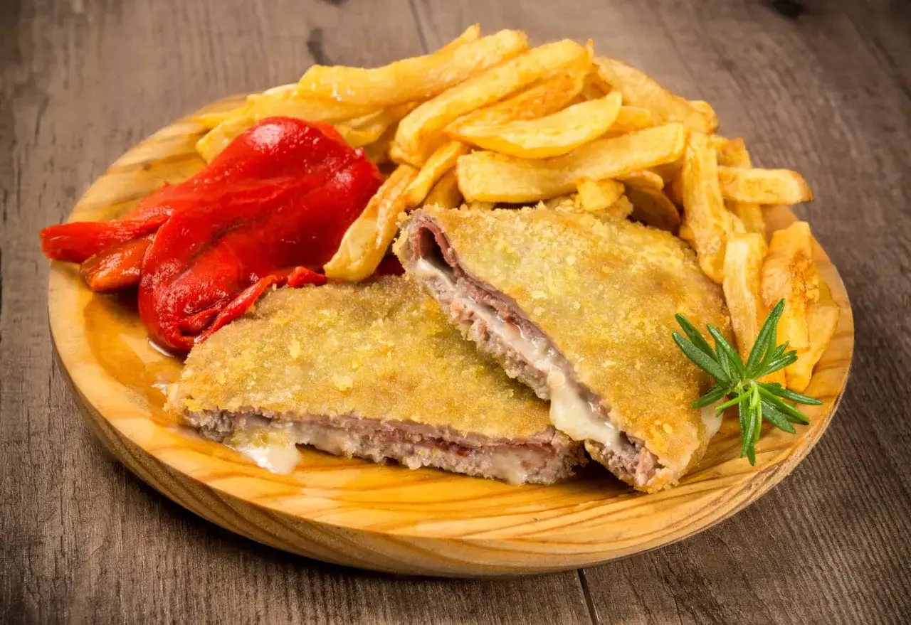 Delicioso cachopo receta, crujiente por fuera y jugoso por dentro, acompa&ntilde;ado de patatas fritas y pimientos asados.