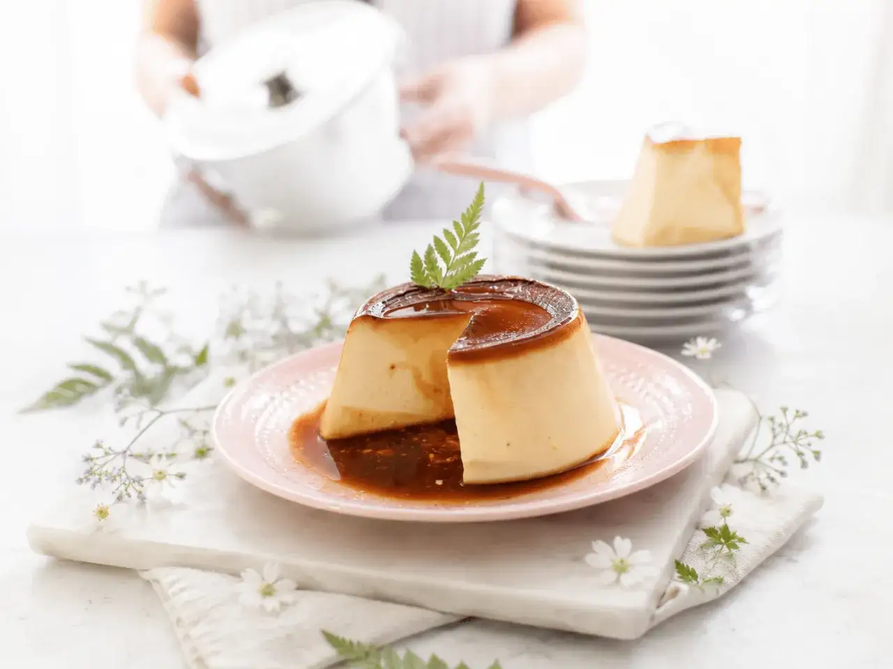 Un delicioso flan de huevo casero, con caramelo l&iacute;quido y decorado con una ramita verde, servido en un plato rosa.