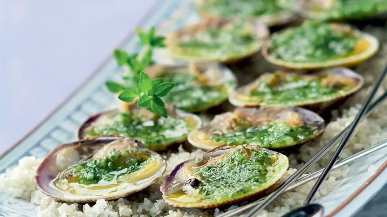 Deliciosos tipos de berberechos gratinados con hierbas, servidos sobre sal gruesa en una bandeja.