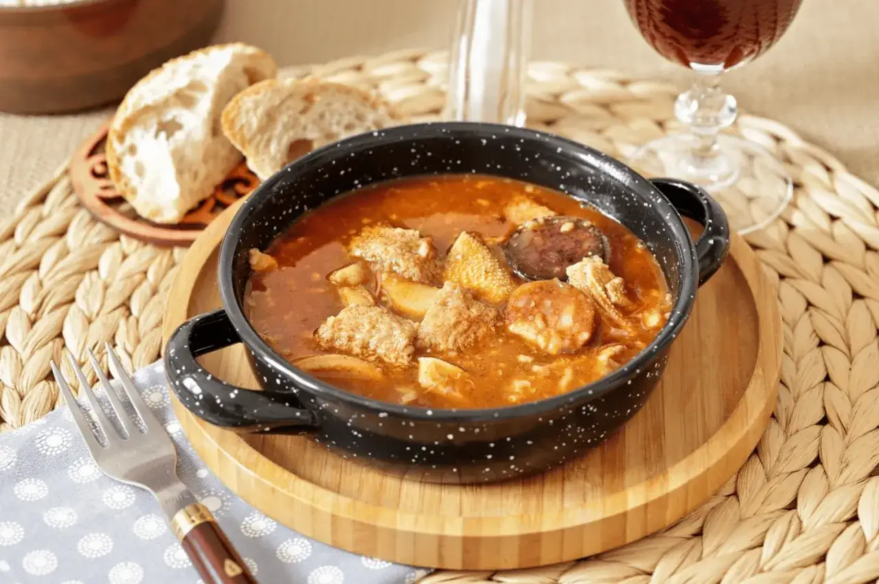 Un plato humeante de callos a la madrileña, con trozos de chorizo y pan rústico al lado, listo para disfrutar.