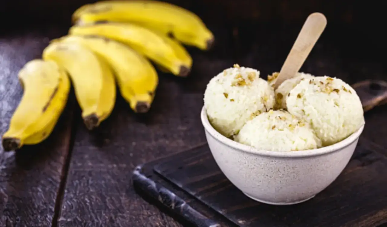Un taz&oacute;n de cremoso helado de pl&aacute;tano con nueces picadas, acompa&ntilde;ado de pl&aacute;tanos frescos en un fondo oscuro.
