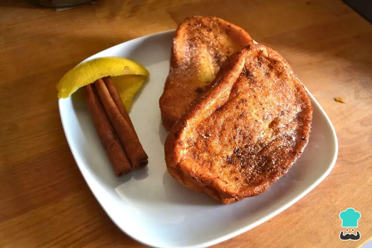 Dos deliciosas torrijas al horno, espolvoreadas con az&uacute;car y canela, acompa&ntilde;adas de una rama de canela y una rodaja de lim&oacute;n.