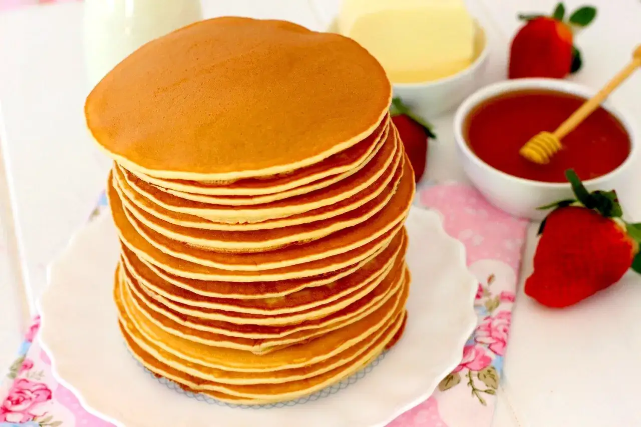 Una torre de tortitas americanas doradas, con fresas, miel y mantequilla, listas para un desayuno delicioso.