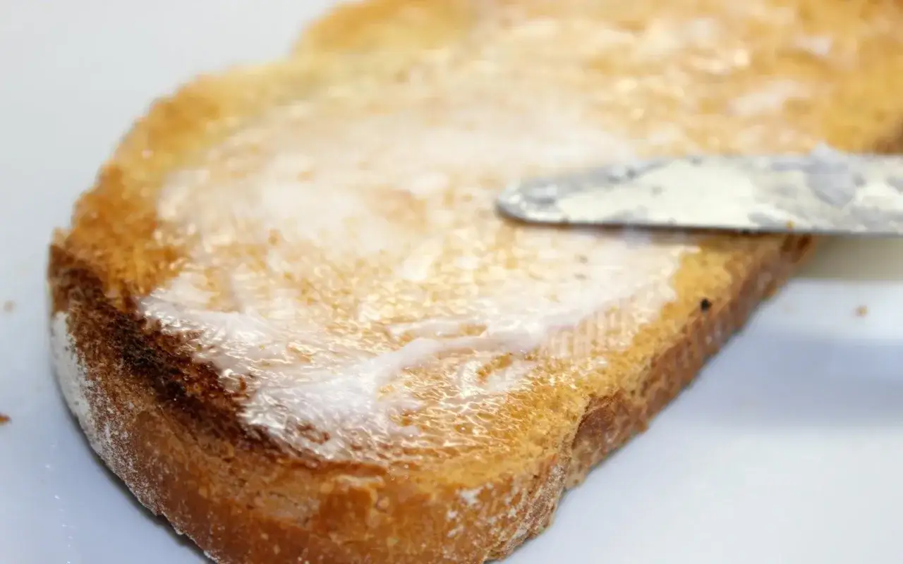 Rebanada de pan tostado con un cuchillo esparciendo manteca. Un delicioso lomo en manteca listo para disfrutar.