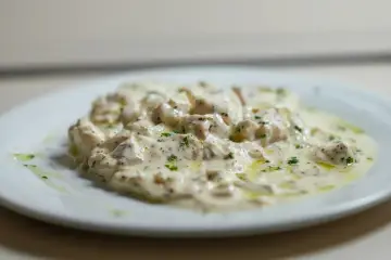 Deliciosa brandada de bacalao cremosa, con trozos de pescado blanco y perejil picado, servida en un plato blanco.
