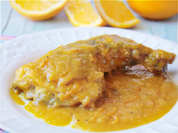 Delicioso pollo a la naranja, bañado en una salsa dorada y jugosa, con gajos de naranja frescos al fondo.