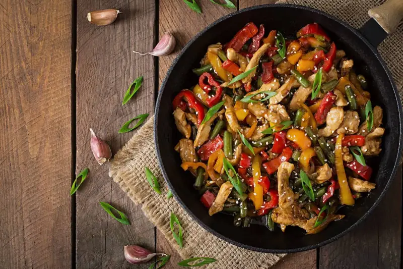 Sabroso wok de pollo con pimientos de colores y judías verdes, espolvoreado con semillas de sésamo y cebolleta.
