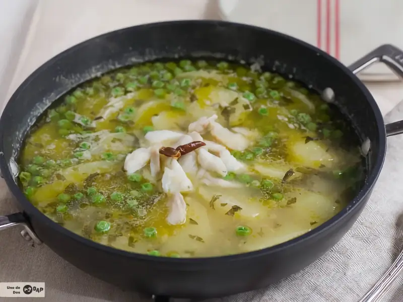 Patatas en salsa verde con trozos de pescado blanco y guisantes, servido en una sartén.