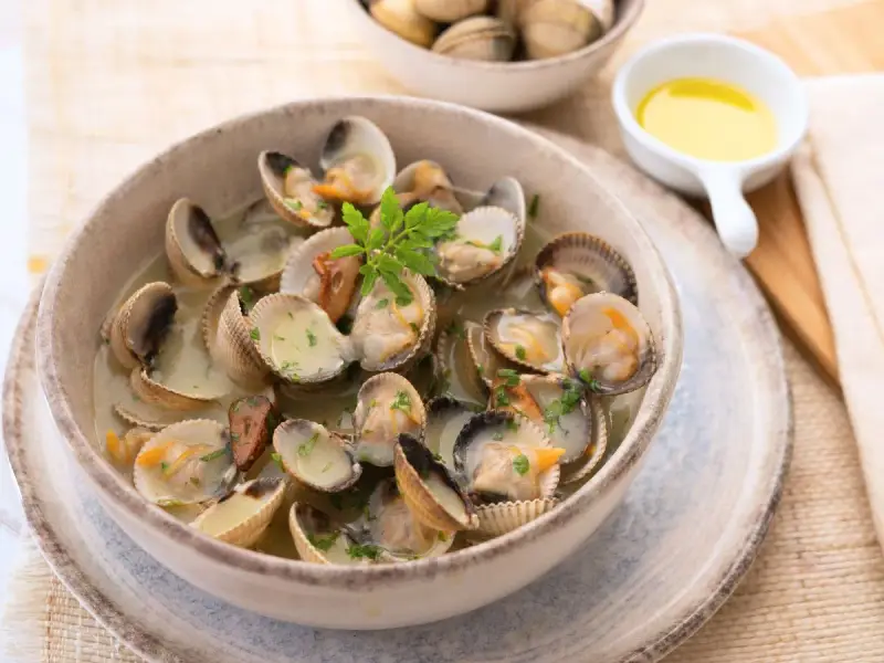Deliciosos tipos de berberechos cocinados en su jugo, servidos en un cuenco de cerámica con perejil picado.